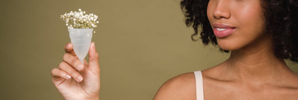 positive young black lady demonstrating menstrual cup in beige studio