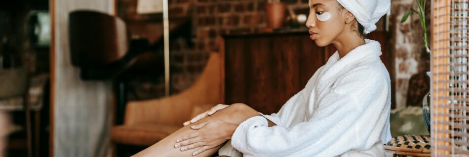 woman in bathrobe applying cream on leg