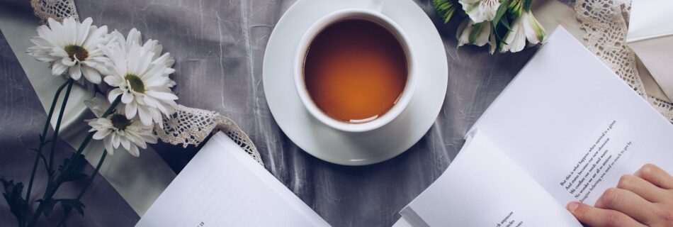 white ceramic teacup with saucer near two books above gray floral textile